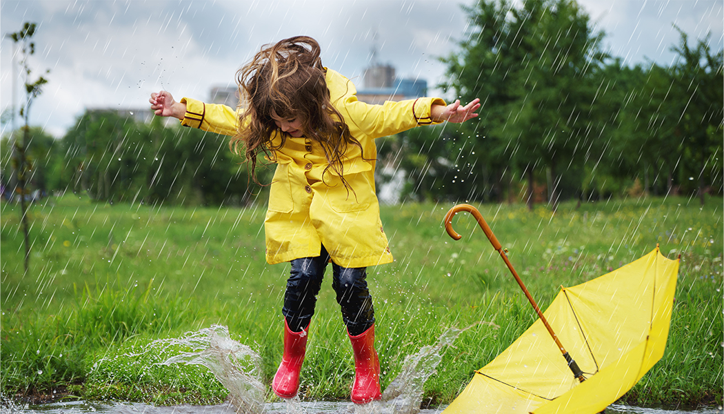 Child jumping in puddles wearing wellies and coat with umbrella as a reminder for professionals and concerned others to help children affected by their parent's drinking have some time for fun