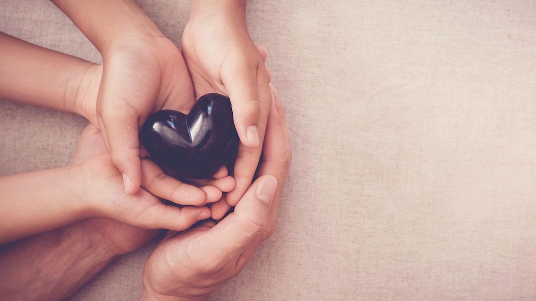 3 pairs of hands around purple heart stone representing professionals or concerned others supporting people affected by their parent's drinking