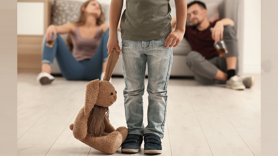 Child holding soft toy bunny for comfort as parents drink alcohol in background