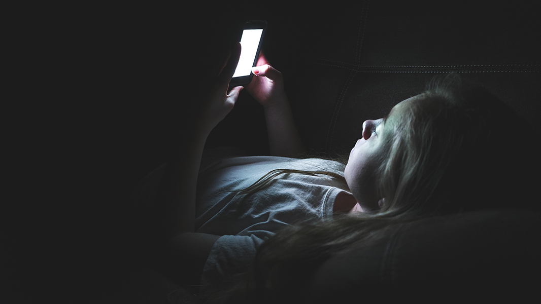 Young person using their mobile phone lying down in the dark to represent young person affected by a parent's drinking receiving support from a professional or concerned other such as a family member or friend
