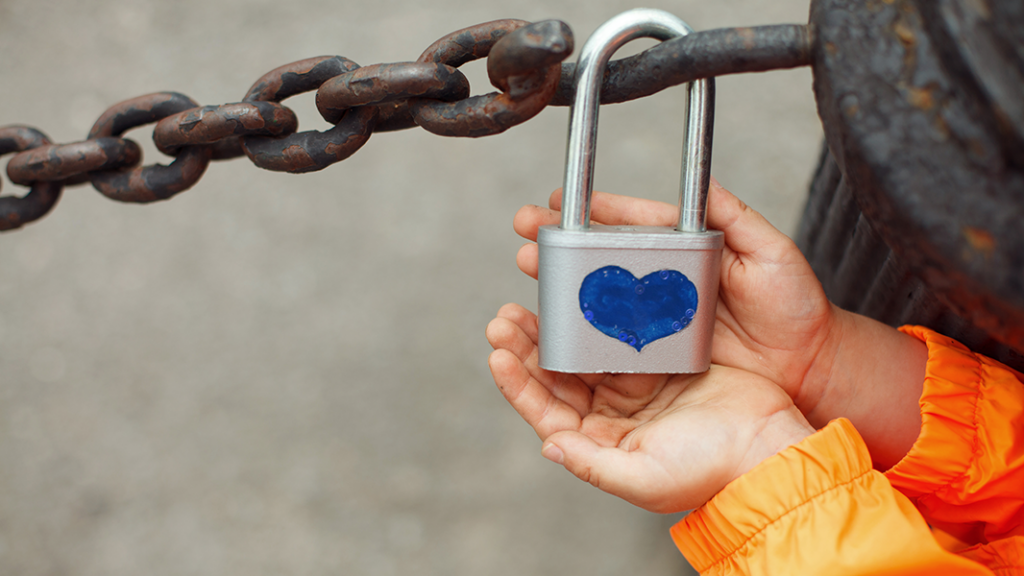 Child holding padlock with blue heart attached to outdoor chain in memory of a parent who died because of their drinking