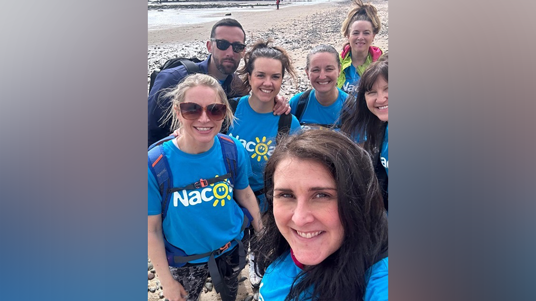 Group of people in blue Nacoa t-shirts on beach walking Northumberland Coast Marathon to fundraise in memory of parent who died from alcoholism