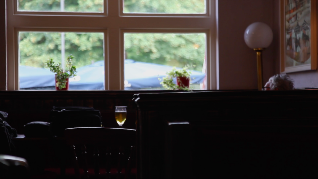 The Summer I made a film about my dad - screenshot from 'Still, life' film by Priya showing a man sitting in a corner of a pub with a pint of beer 