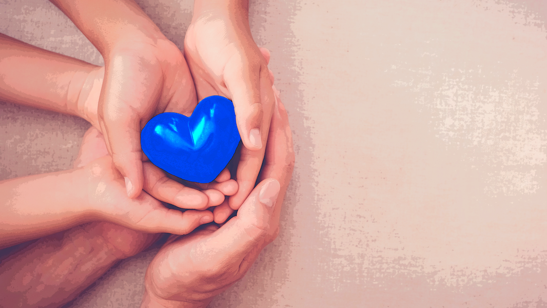 Three people's hands holding a blue heart to represent teachers supporting children affected by their parents' drinking