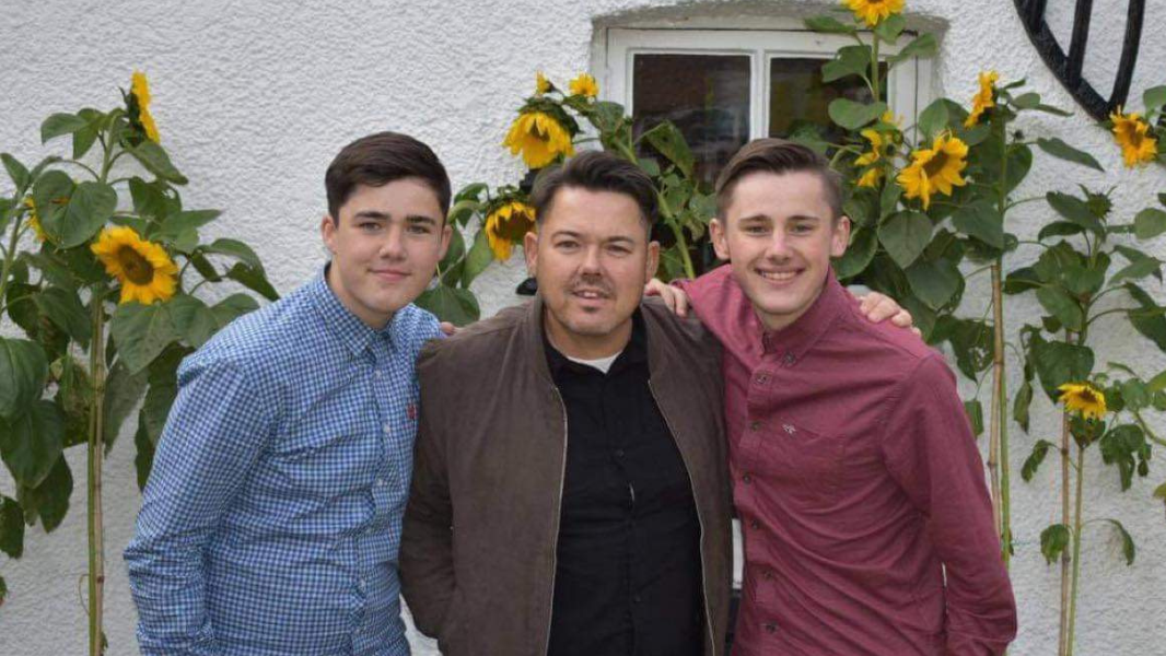 Charlie and Quinn standing in front of sunflowers with their dad Karlos who died from cirrhosis