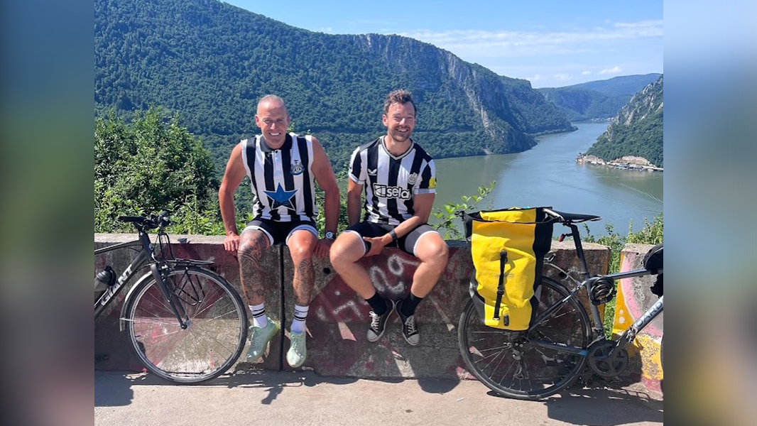 Paul and his dad wearing Newcastle United football shirts sat on bridge over river during cycle from Newcastle to Istanbul to show that if you grow up with an alcoholic parent, you can do anything